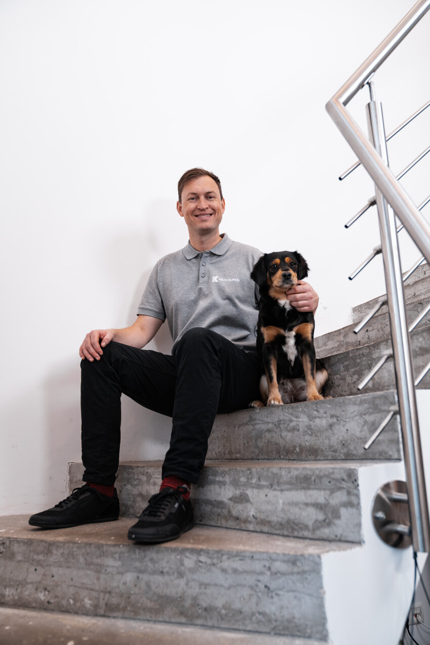 Christian Schimonek sitzt mit seinem Hund auf der Treppe im Firmengebäude